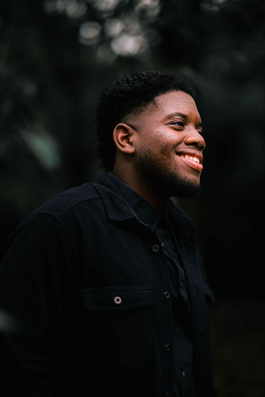 Portrait of a young man smiling warmly in an outdoor setting, exuding positivity.