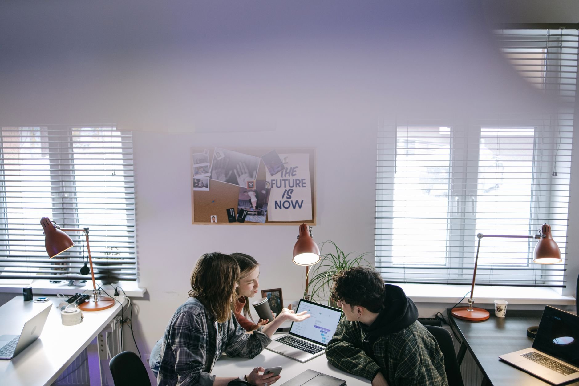 A group of people discussing ideas around laptops in a bright, modern office space.